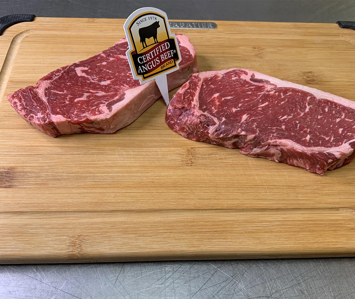 Photo of two Certified Angus steaks sitting atop a wood cutting board with a Certified Angus Beef Brand sign
